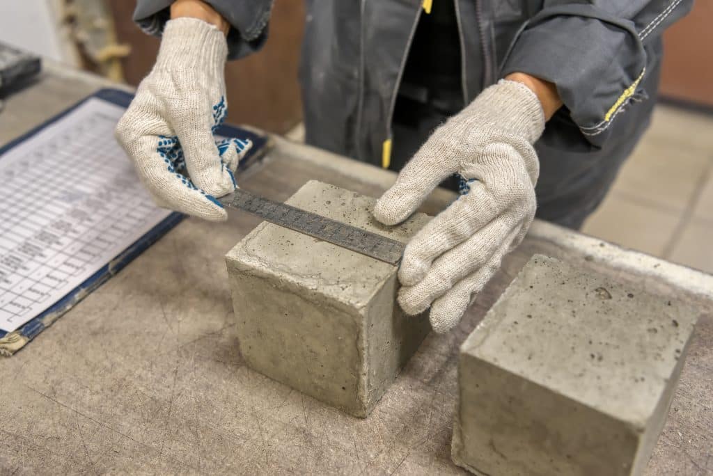 Lab technician measures the size of a concrete cube using a metal ruler.