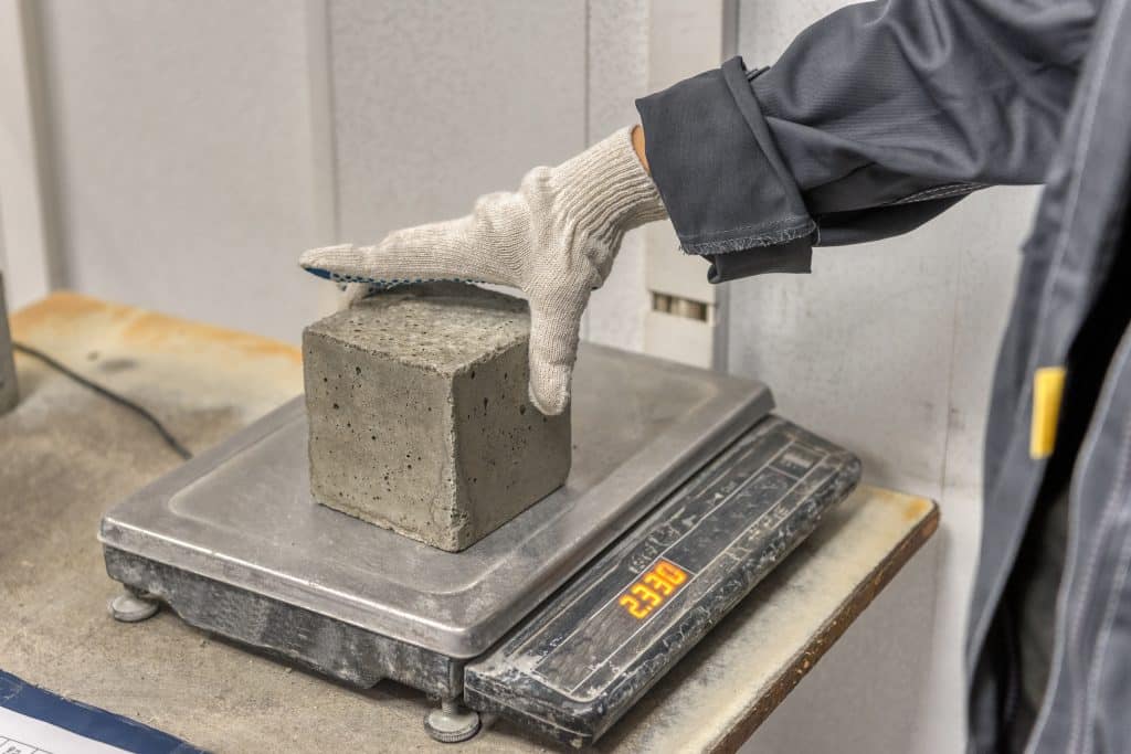 Laboratory for testing building materials. Laboratory assistant weighs a concrete cube on an electronic scale.